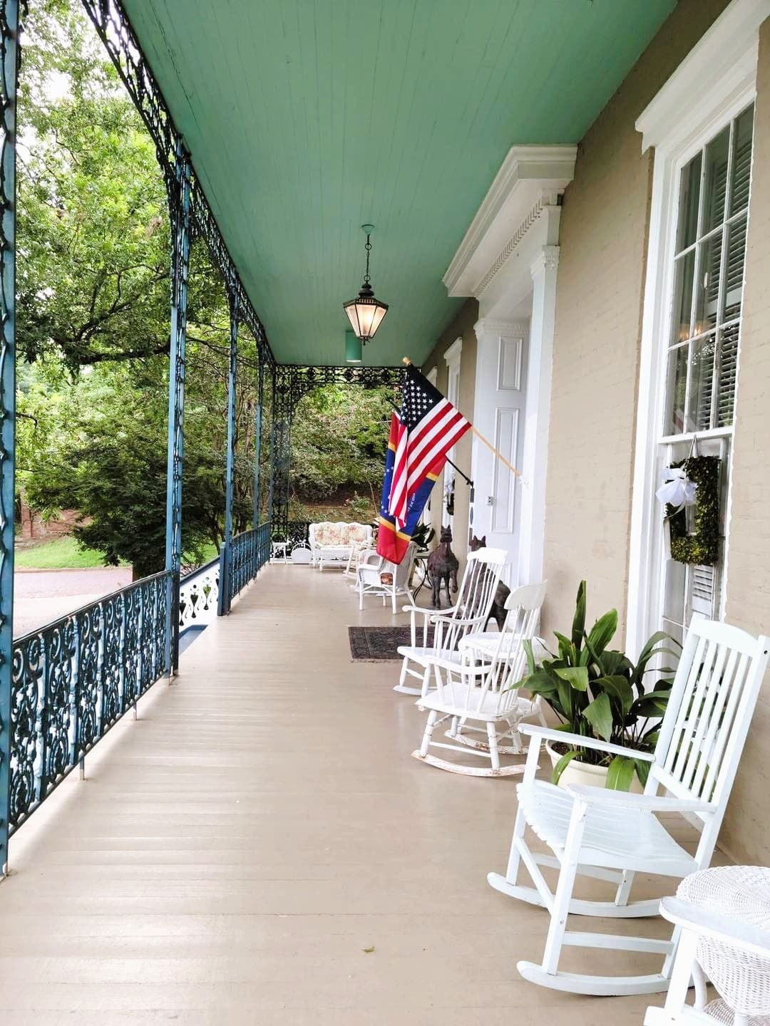 A cozy porch with rocking chairs, hanging lanterns, and flags, surrounded by greenery.