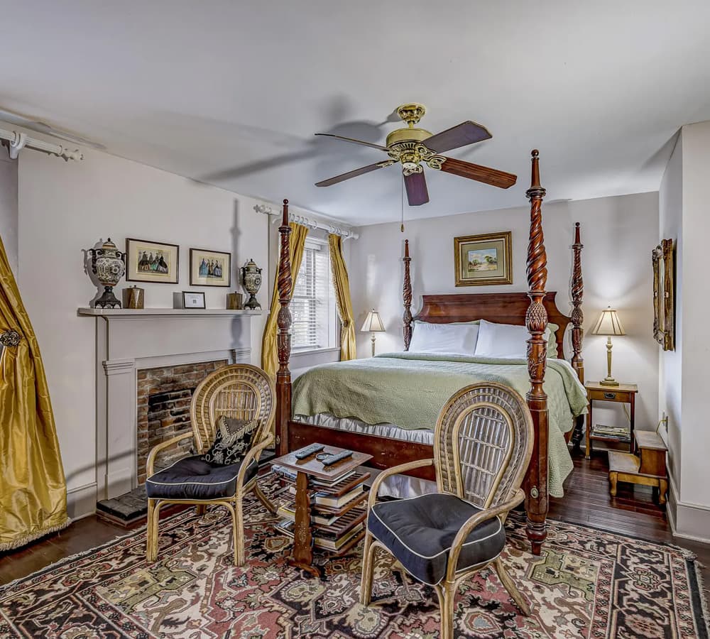 A cozy bedroom featuring a four-poster bed, decorative chair, and a fireplace.